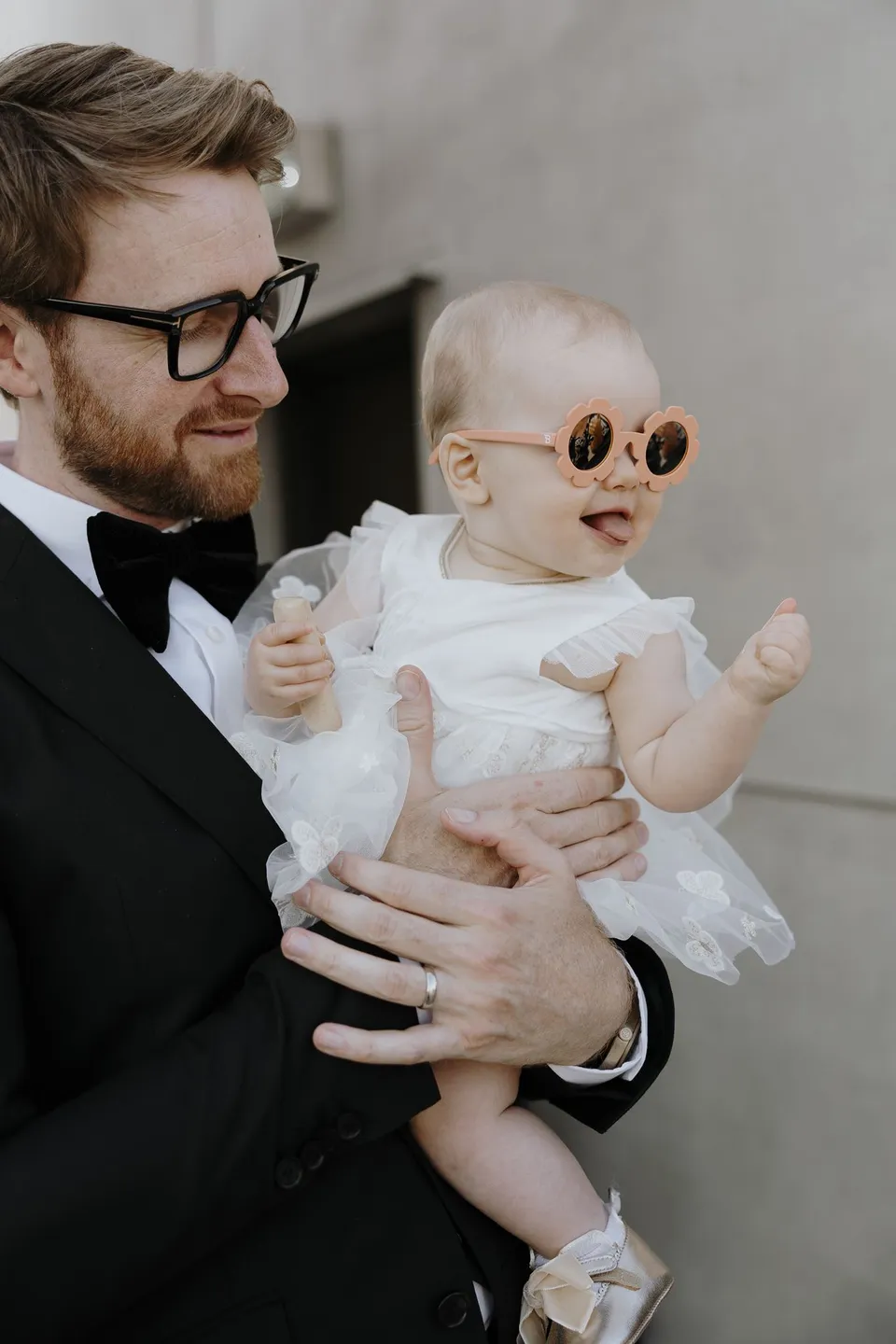 Adam holding a baby wearing round sunglasses and a white outfit, during Danielle and Adam’s Elopement Collective elopement at The Calile Hotel in Fortitude Valley, Brisbane.