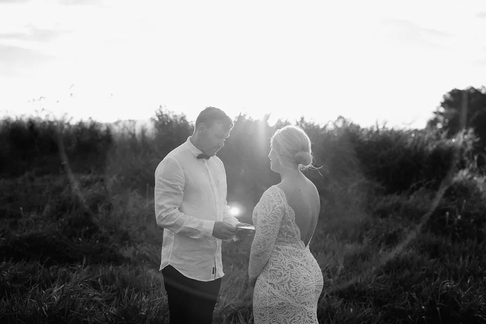 A black and white view of Matt reading his vows to Laura with sunlight behind them, in the Tweed Valley, NSW, for an Elopement Collective elopement. Photo by Bulb Creative.