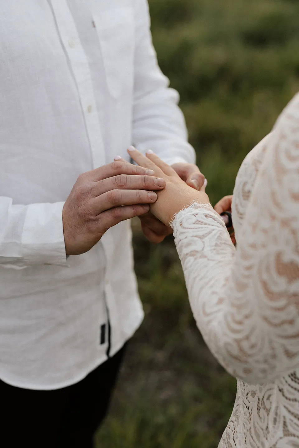Matt placing a wedding ring on Laura’s finger, with her lace sleeve visible against the green grass, in the Tweed Valley, NSW, for an Elopement Collective elopement. Photo by Bulb Creative.