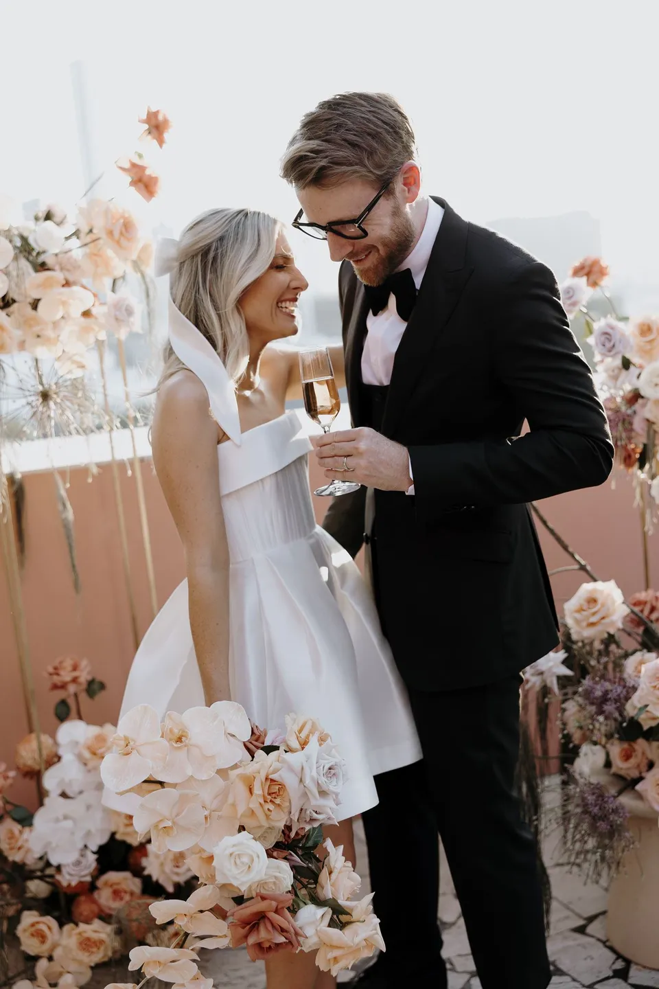 Danielle and Adam celebrating with champagne beside peach and white flowers at The Calile Hotel in Fortitude Valley, Brisbane, after their Elopement Collective ceremony.