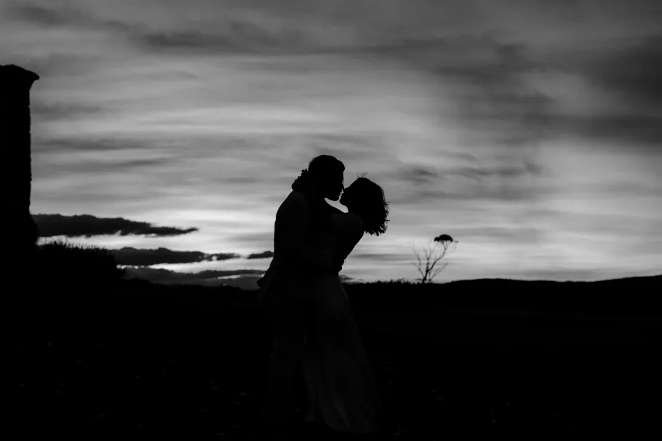 Black and white silhouette of the couple leaning close beneath the evening clouds, at Thalia Haven on the East Coast of Tasmania, Australia, for an Elopement Collective elopement. Photograph by Joey Willis.