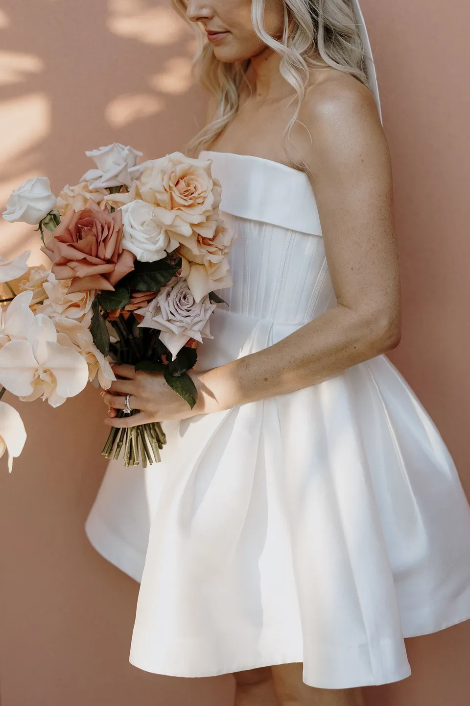 Close view of Danielle’s structured white dress and bouquet of peach roses and pale orchids, during Danielle and Adam’s Elopement Collective elopement at The Calile Hotel in Fortitude Valley, Brisbane.