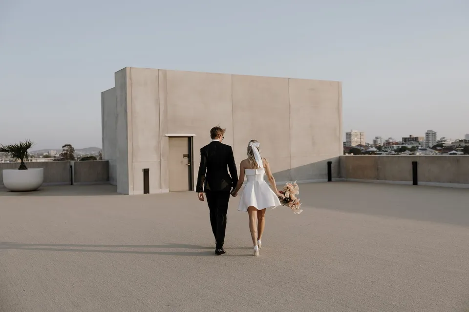 Danielle and Adam walking away hand in hand across the open hotel rooftop, during Danielle and Adam’s Elopement Collective elopement at The Calile Hotel in Fortitude Valley, Brisbane.