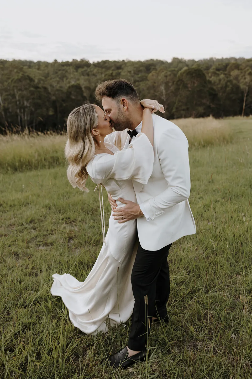 Greg holding Gabrielle in his arms as they kiss in the green paddock at Roundhill Retreat in Obi Obi, Sunshine Coast Hinterland, for their Elopement Collective elopement.