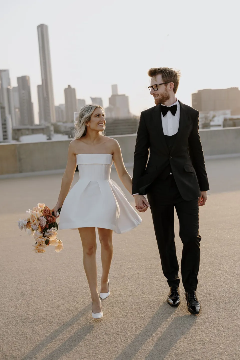 Danielle and Adam looking at each other as they walk hand in hand with Brisbane’s skyline behind them, during Danielle and Adam’s Elopement Collective elopement at The Calile Hotel in Fortitude Valley, Brisbane.