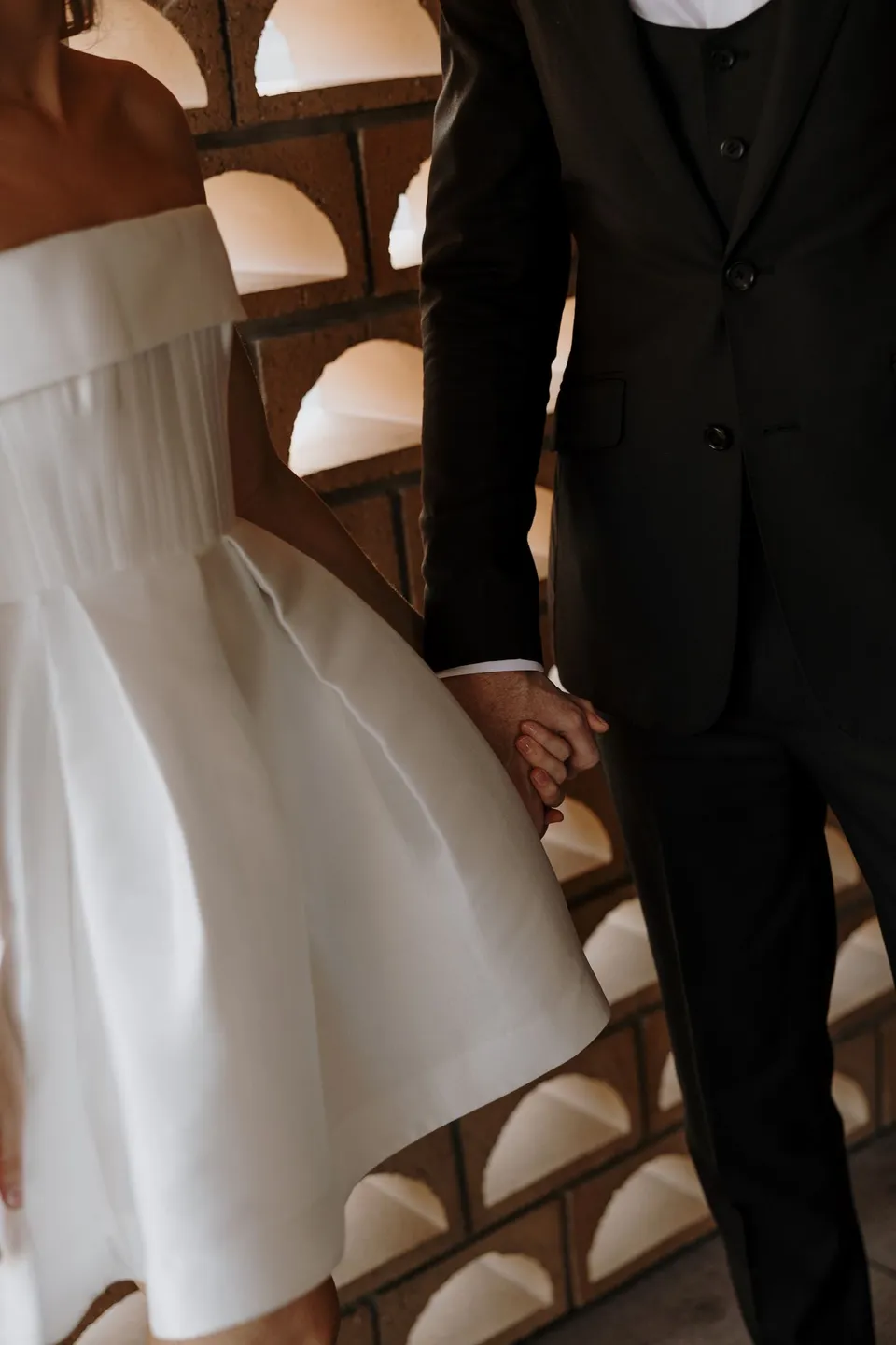 Close view of Danielle and Adam holding hands beside an arched brick screen, during Danielle and Adam’s Elopement Collective elopement at The Calile Hotel in Fortitude Valley, Brisbane.