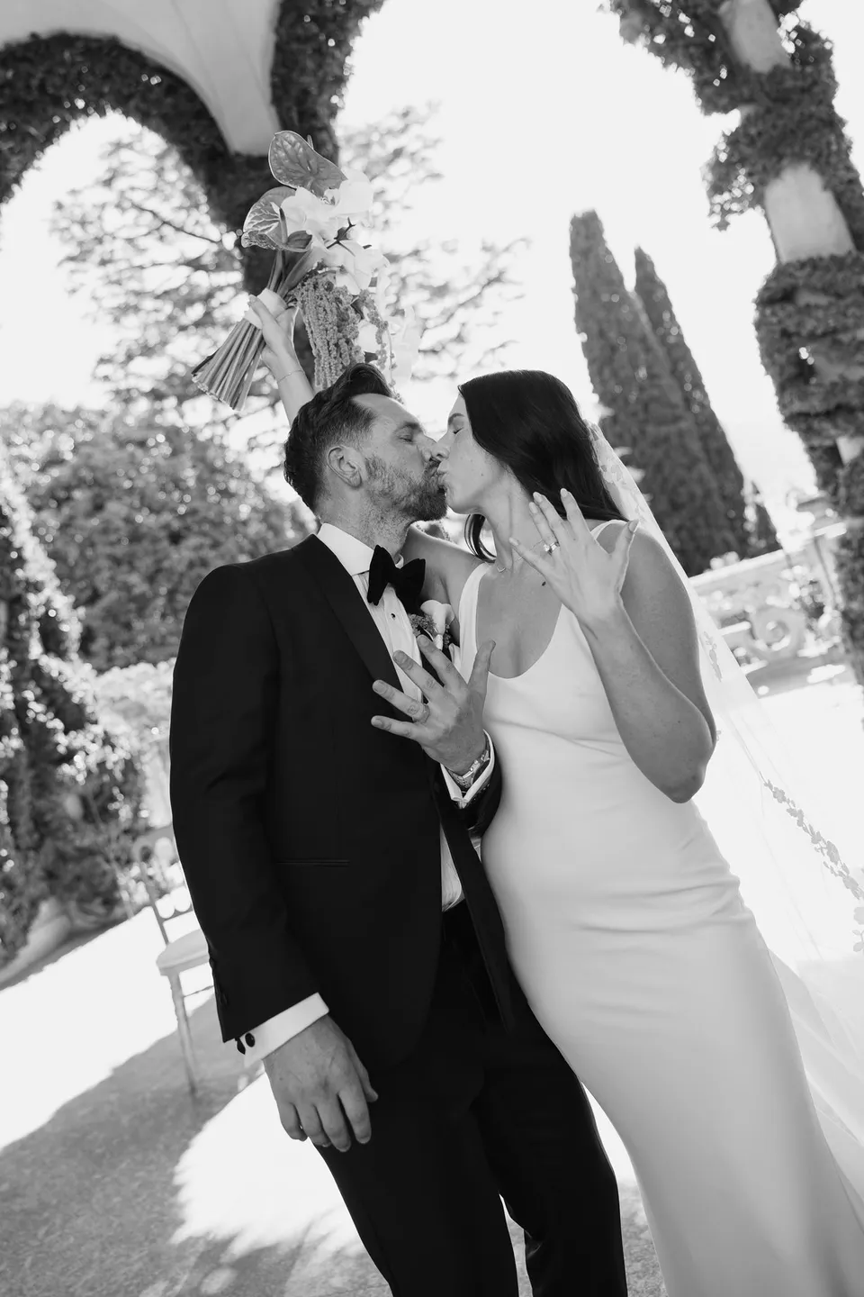 Black and white photograph of Lyndal and Lachlan kissing beneath Villa del Balbianello’s ivy-covered loggia, at Lake Como in Lombardy, Italy, for an Elopement Collective elopement. Photograph by George Bowden.
