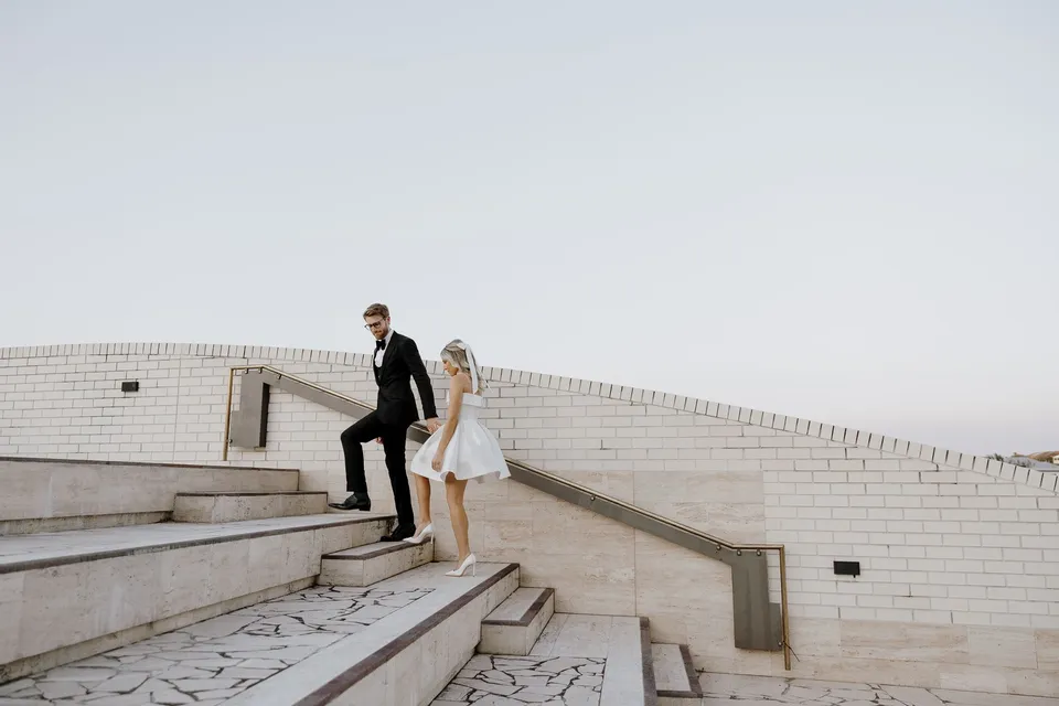 Danielle and Adam climbing wide stone steps bordered by white brick, during Danielle and Adam’s Elopement Collective elopement at The Calile Hotel in Fortitude Valley, Brisbane.