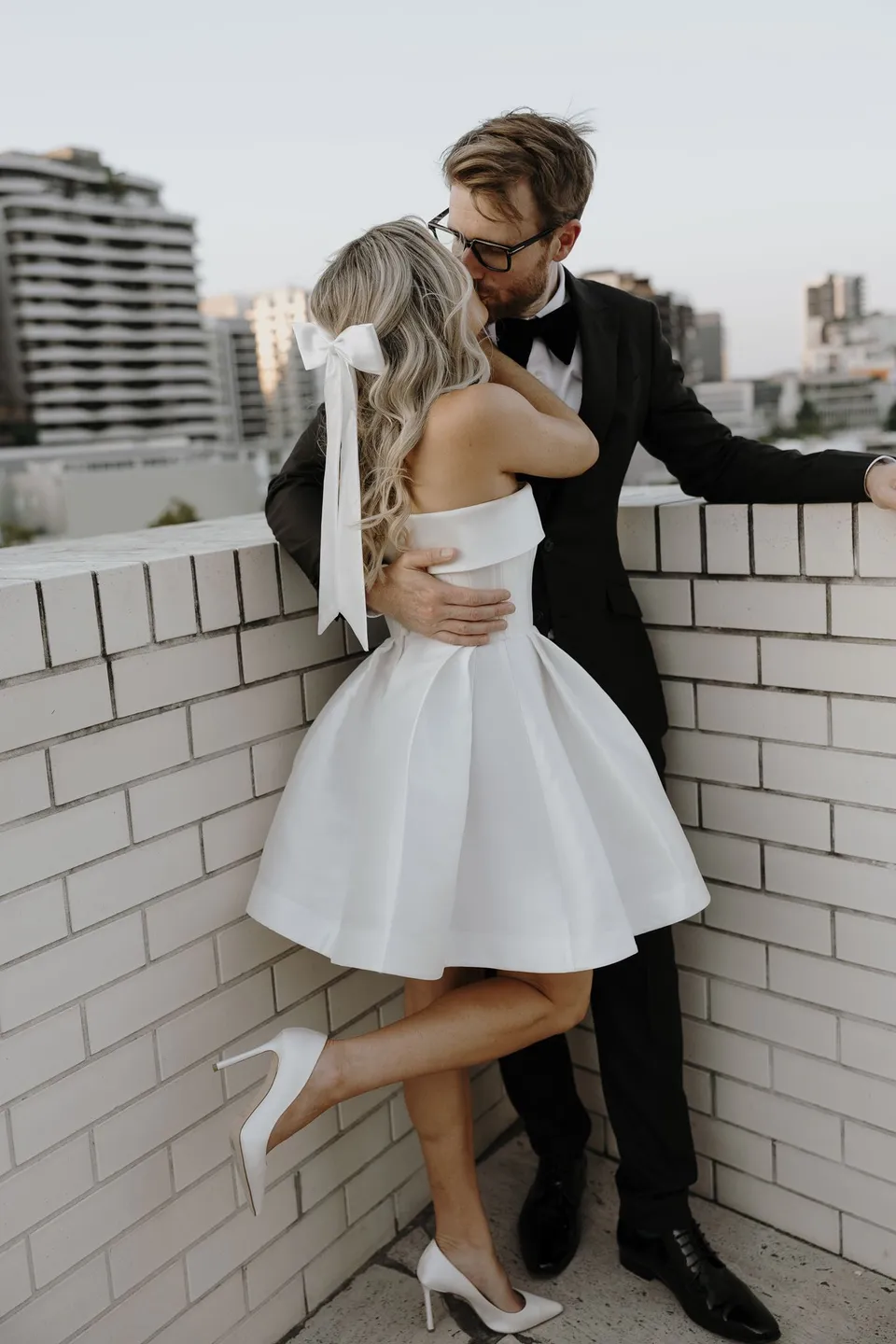 Danielle and Adam embracing beside a white brick balustrade with Brisbane beyond, during Danielle and Adam’s Elopement Collective elopement at The Calile Hotel in Fortitude Valley, Brisbane.