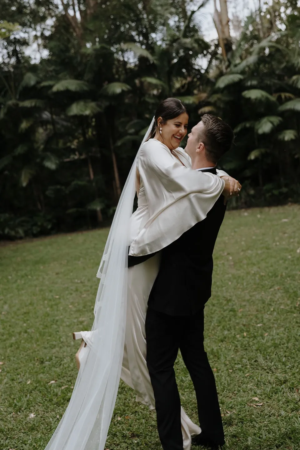 Matthew lifting Laura into his arms in the garden. At Fig Tree Villa in Ewingsdale, Byron Bay, for an Elopement Collective elopement. Photograph by George Bowden.