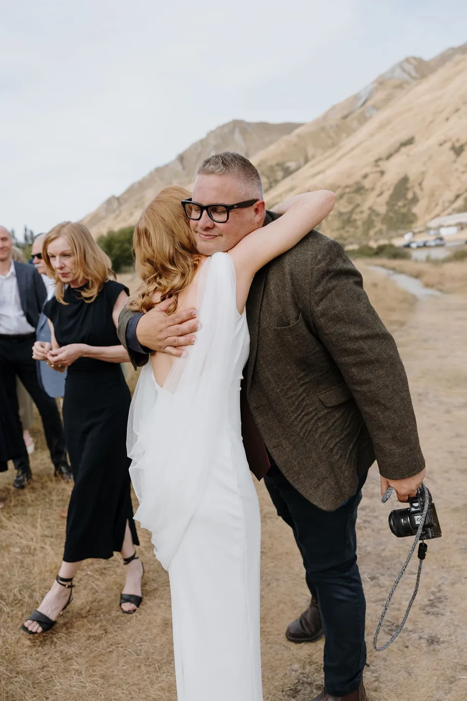 Neve hugging celebrant Josh Withers after the ceremony beside the lake, at Moke Lake in Queenstown, New Zealand, for an Elopement Collective Queenstown elopement. Photo by George Bowden.