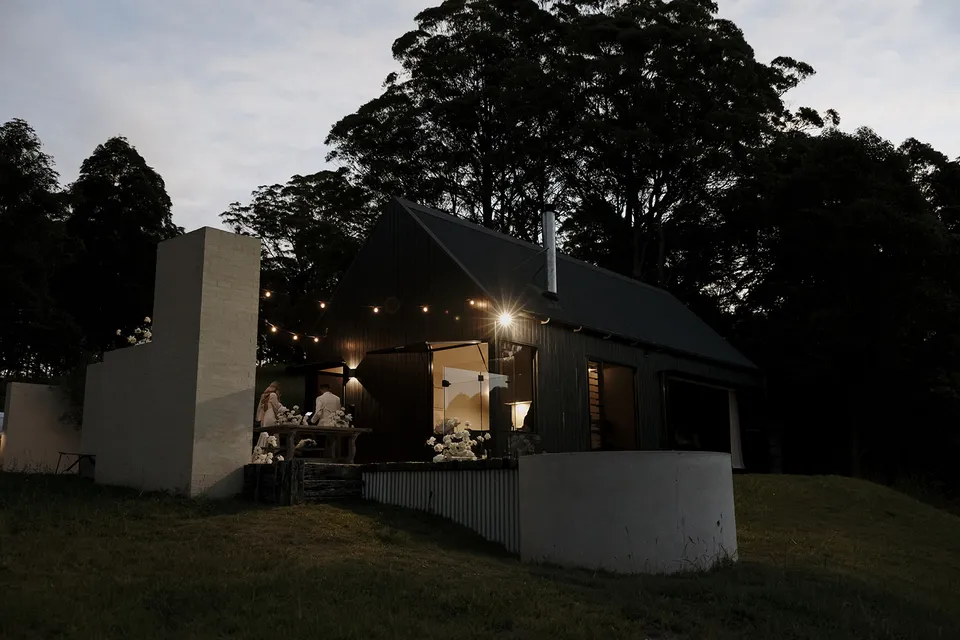 Roundhill Retreat’s cabin glowing beneath festoon lights at dusk, with white flowers in the courtyard after Gabrielle and Greg’s Elopement Collective elopement in Obi Obi, Sunshine Coast Hinterland.