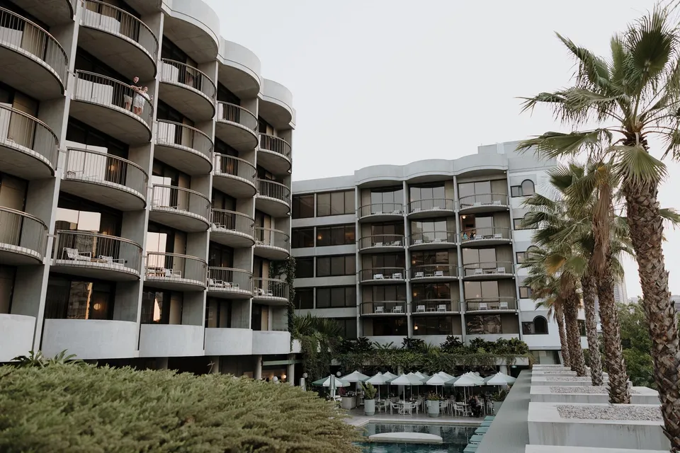 The Calile Hotel’s curved balconies, pool and palm trees viewed from above, during Danielle and Adam’s Elopement Collective elopement at The Calile Hotel in Fortitude Valley, Brisbane.