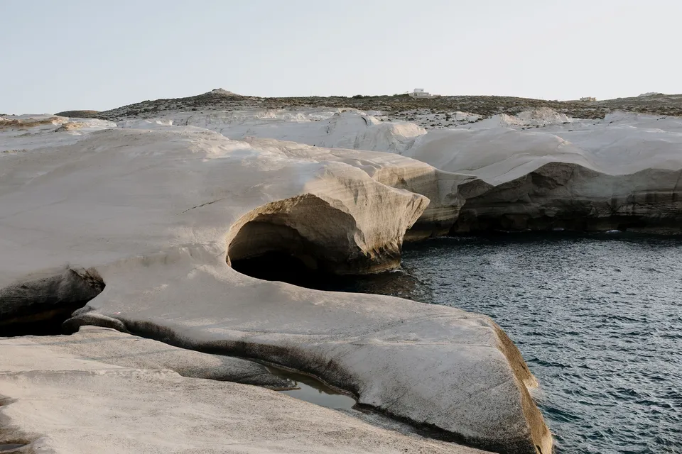 A white coastal rock arch and headland surrounded by deep blue water, at Sarakiniko on Milos in the Cyclades, Greece, during an Elopement Collective elopement. Photograph by George Bowden.