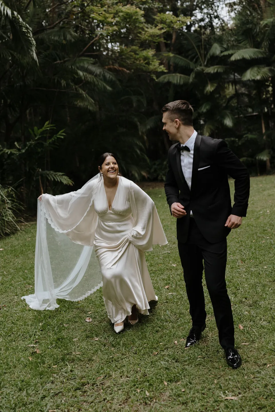 Laura and Matthew running hand in hand across the lawn. At Fig Tree Villa in Ewingsdale, Byron Bay, for an Elopement Collective elopement. Photograph by George Bowden.