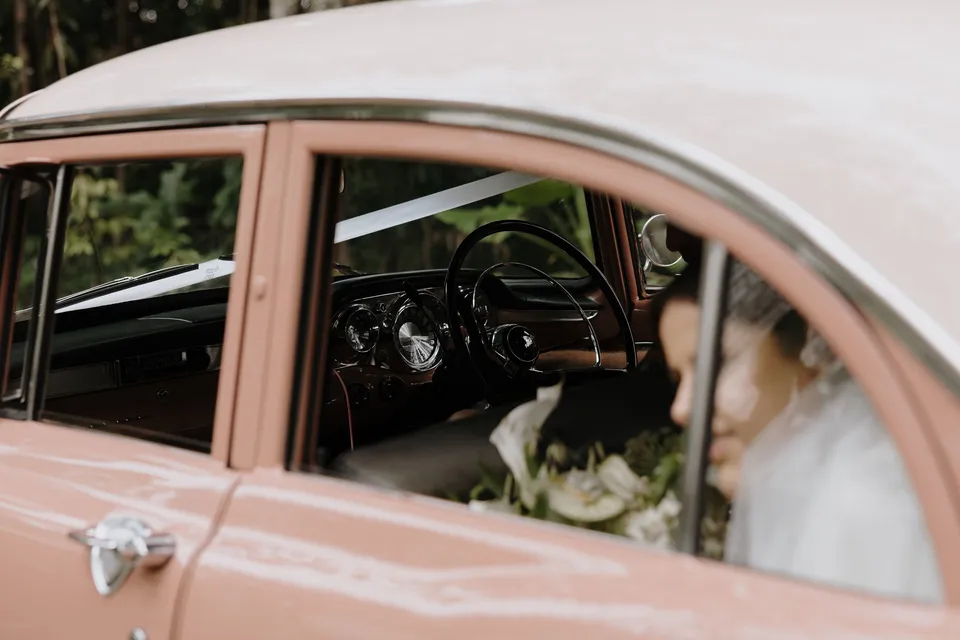 Laura smiling from the window of the pink vintage Holden from May The E.K. In the Byron Bay region of northern New South Wales, for an Elopement Collective elopement. Photograph by George Bowden.