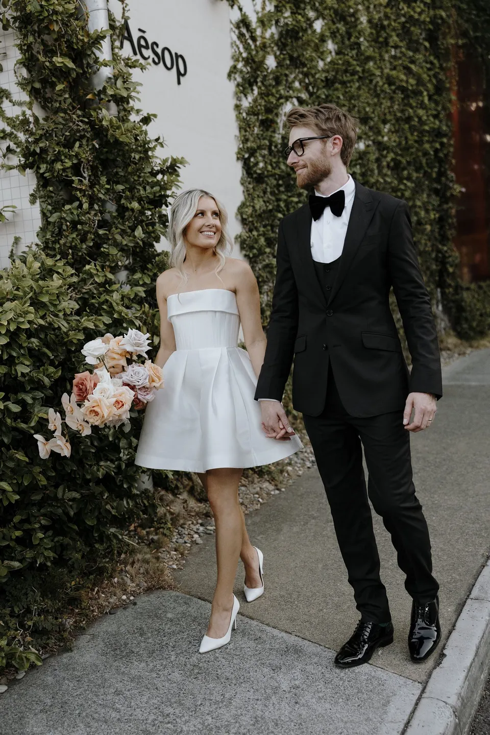 Danielle and Adam laughing and holding hands beside an ivy wall in the James Street precinct, during Danielle and Adam’s Elopement Collective elopement at The Calile Hotel in Fortitude Valley, Brisbane.