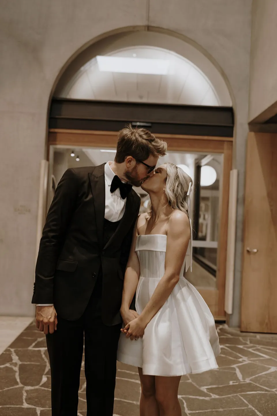 Danielle and Adam kissing beneath a stone arch in the hotel corridor, during Danielle and Adam’s Elopement Collective elopement at The Calile Hotel in Fortitude Valley, Brisbane.