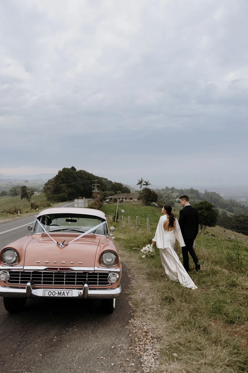 Laura and Matthew beside the pink vintage Holden at a country lookout. In the Byron Bay region of northern New South Wales, for an Elopement Collective elopement. Photograph by George Bowden.