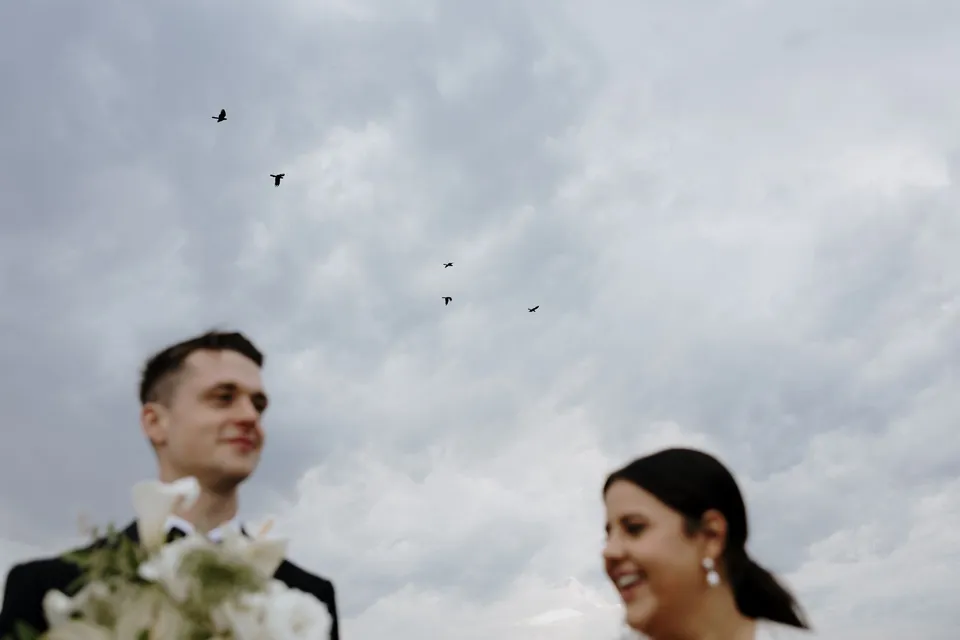 Low-angle portrait of Laura and Matthew smiling beneath birds in the open sky. In the Byron Bay region of northern New South Wales, for an Elopement Collective elopement. Photograph by George Bowden.