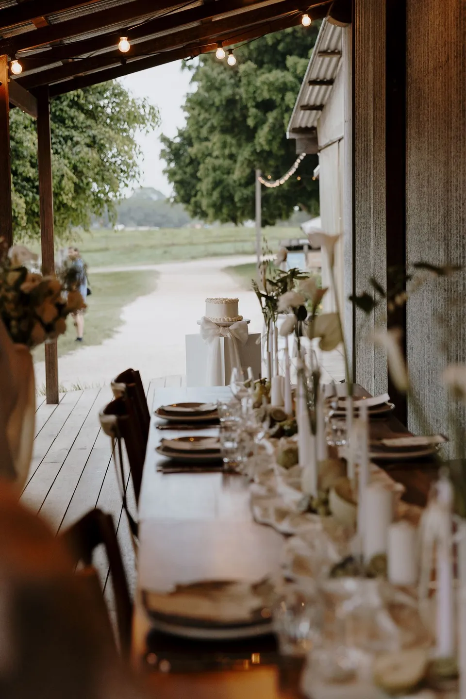 A long reception table set with pale linen, candles and flowers on a covered deck. At The Farm and Three Blue Ducks in Ewingsdale, Byron Bay, for an Elopement Collective elopement. Photograph by George Bowden.