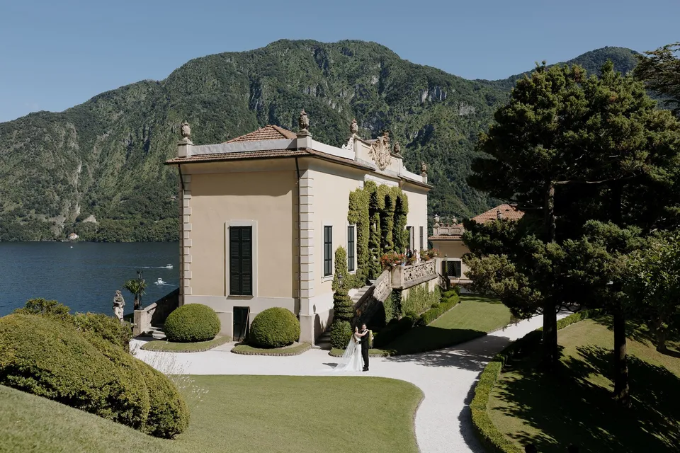 Villa del Balbianello’s pale buildings, rounded hedges and terraced gardens beside the lake, with mountains across the water, at Lake Como in Lombardy, Italy, for an Elopement Collective elopement. Photograph by George Bowden.
