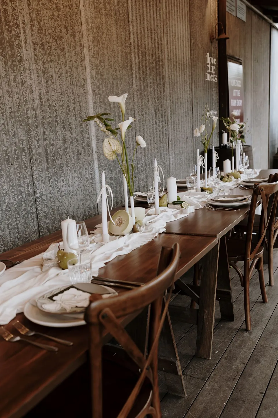 Wooden chairs and a long candlelit table prepared for the couple's reception. At The Farm and Three Blue Ducks in Ewingsdale, Byron Bay, for an Elopement Collective elopement. Photograph by George Bowden.