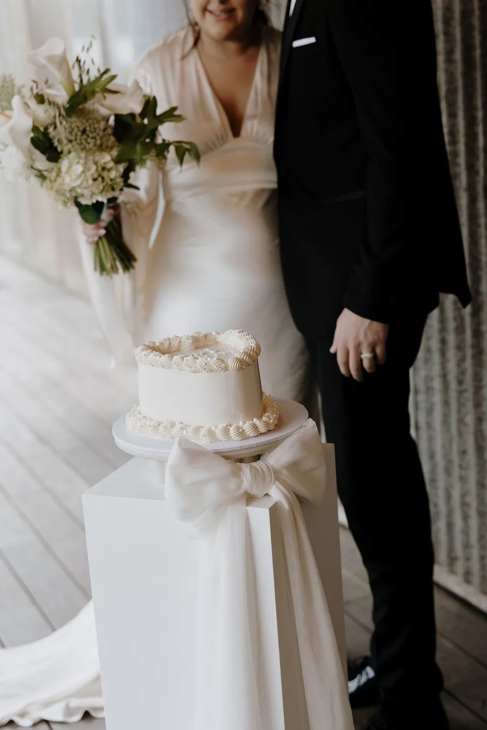 Laura and Matthew standing beside their small white wedding cake. At The Farm and Three Blue Ducks in Ewingsdale, Byron Bay, for an Elopement Collective elopement. Photograph by George Bowden.