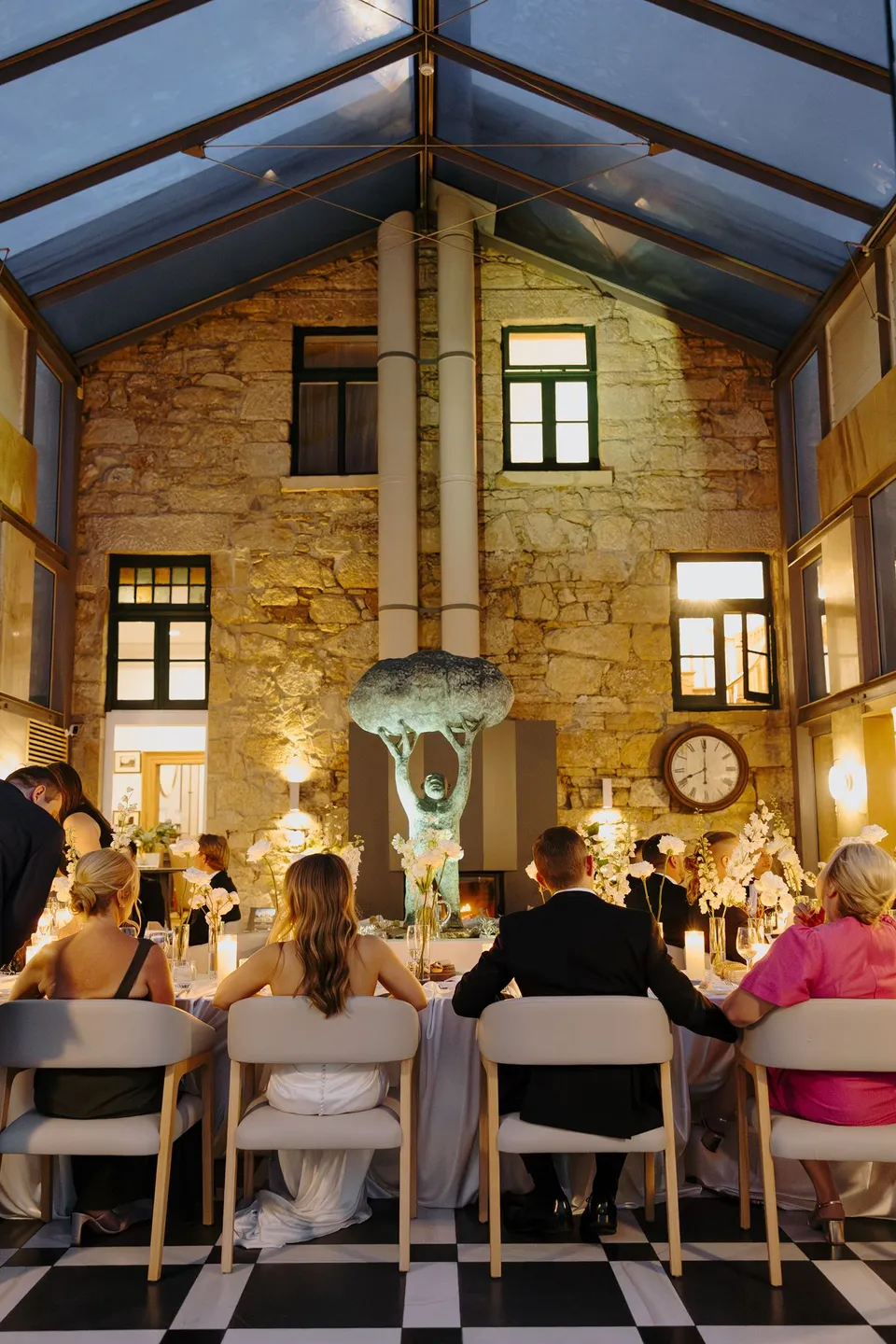 Guests sharing dinner around candlelit tables styled by Artaud & Co beneath the conservatory’s glass roof and stone walls, at Islington Hotel in South Hobart, Tasmania, Australia, for an Elopement Collective summer elopement. Photograph by George Bowden.
