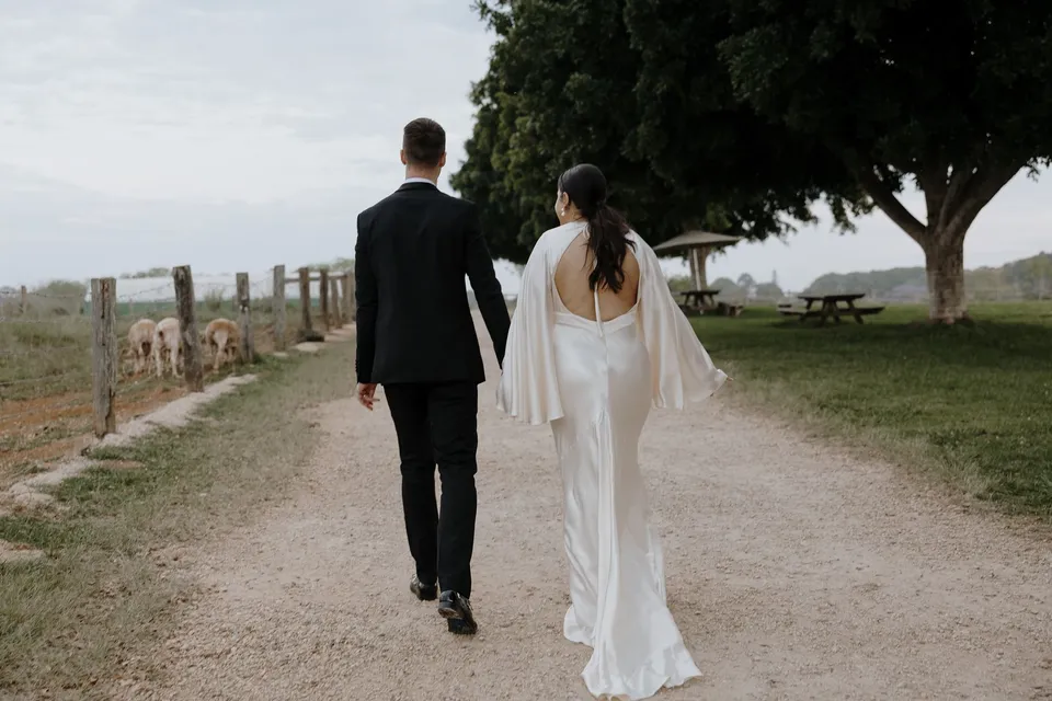Laura and Matthew walking hand in hand along a farm track. At The Farm and Three Blue Ducks in Ewingsdale, Byron Bay, for an Elopement Collective elopement. Photograph by George Bowden.