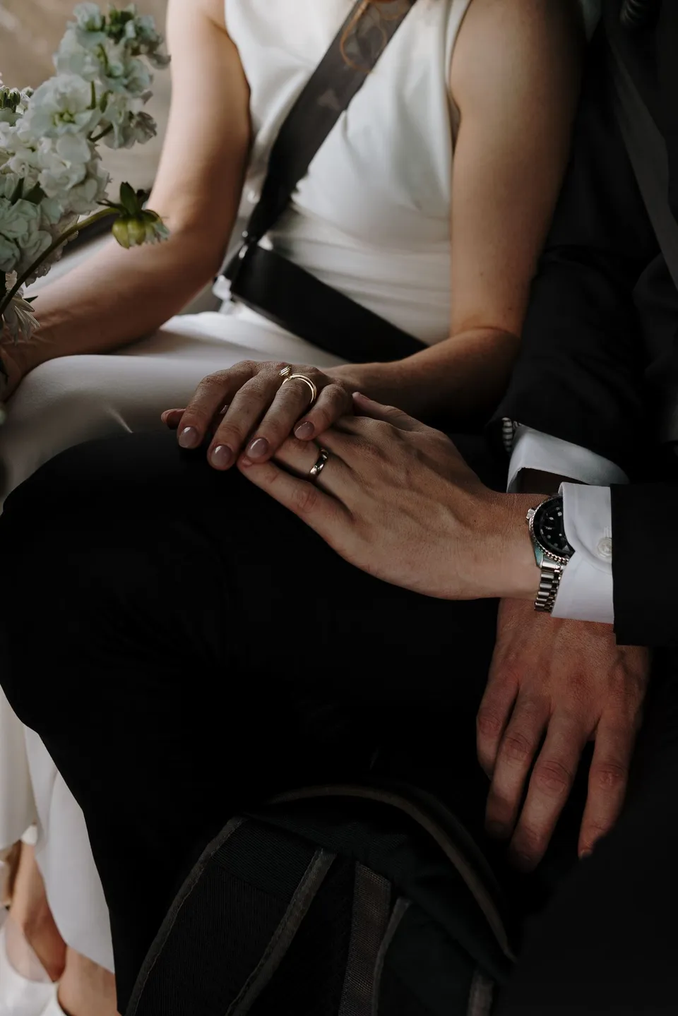 A close-up of Neve and Hamish’s hands and wedding rings inside the helicopter, with part of the white Orange Blossom bouquet visible, above Queenstown, New Zealand, for an Elopement Collective Queenstown elopement. Photo by George Bowden.