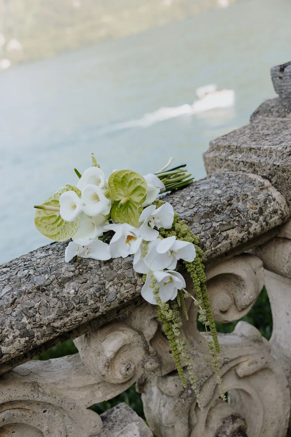 White calla lilies, heart-shaped white blooms and trailing greenery by Garden of Love resting on a carved stone balustrade at Villa del Balbianello above the lake, at Lake Como in Lombardy, Italy, for an Elopement Collective elopement. Photograph by George Bowden.