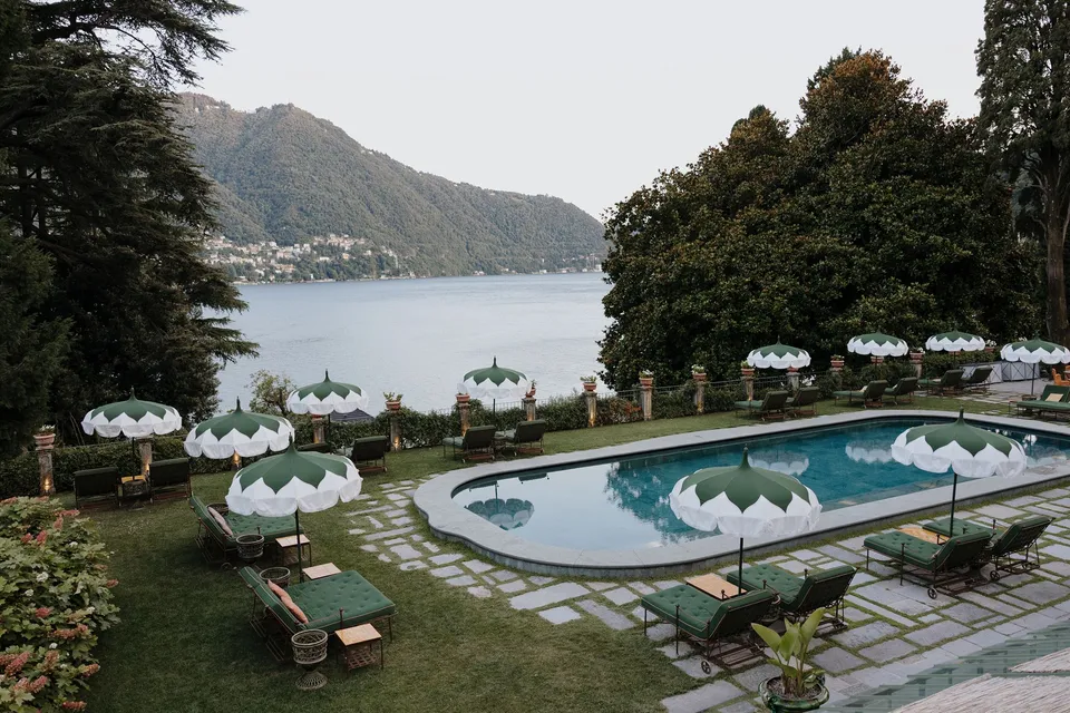 Passalacqua’s outdoor pool, green loungers and scalloped white parasols overlooking the lake and the mountains beyond, at Passalacqua in Moltrasio, Lake Como, Italy, for an Elopement Collective elopement. Photo by George Bowden.