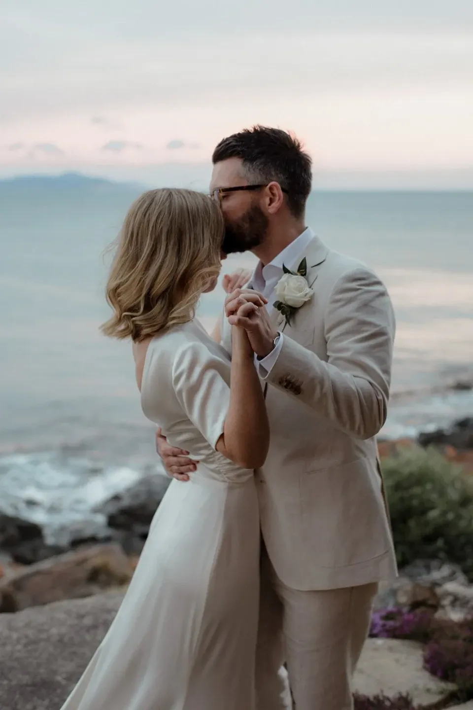 A couple dance close together beside the sea in soft evening light.