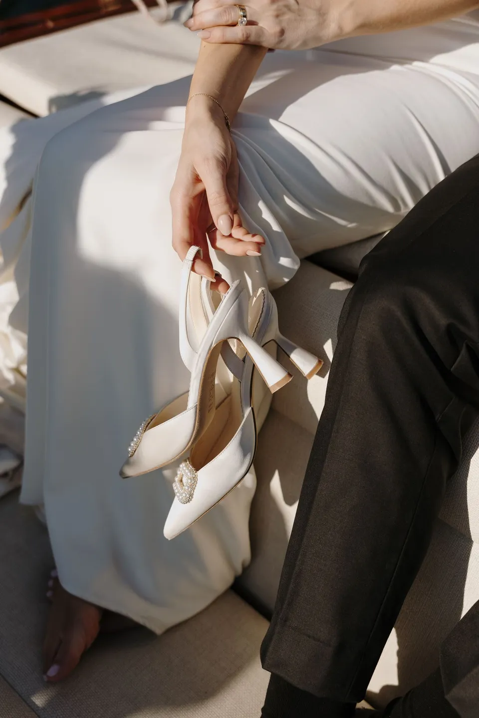 Close view of Lyndal and Lachlan holding hands on a boat, with Lyndal carrying her white heels in her other hand, at Lake Como in Lombardy, Italy, for an Elopement Collective elopement. Photograph by George Bowden.
