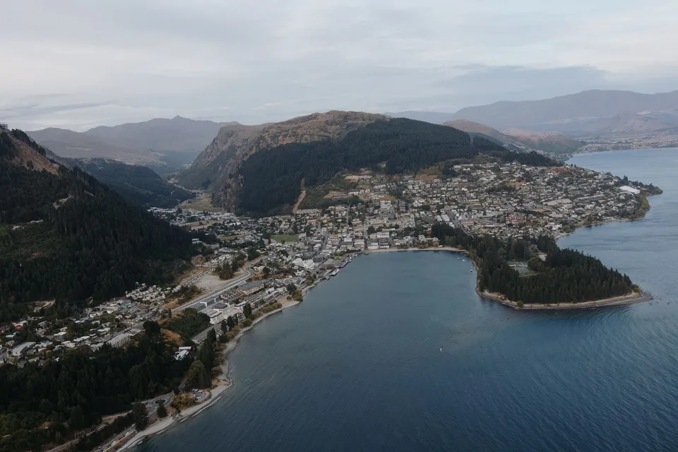 An aerial view of Queenstown’s lakefront, wooded peninsula and hillside neighbourhoods beside Lake Wakatipu, in Queenstown, New Zealand, for an Elopement Collective Queenstown elopement. Photo by George Bowden.