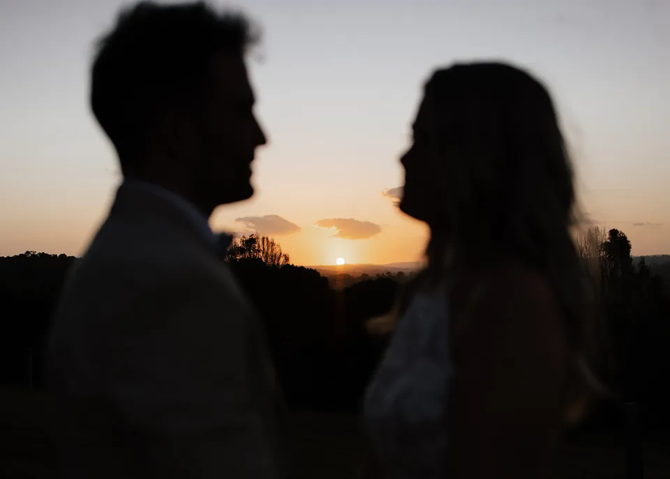 A couple facing each other in silhouette as the sun sets over rolling hills in Byron Bay, New South Wales, during an Elopement Collective elopement.