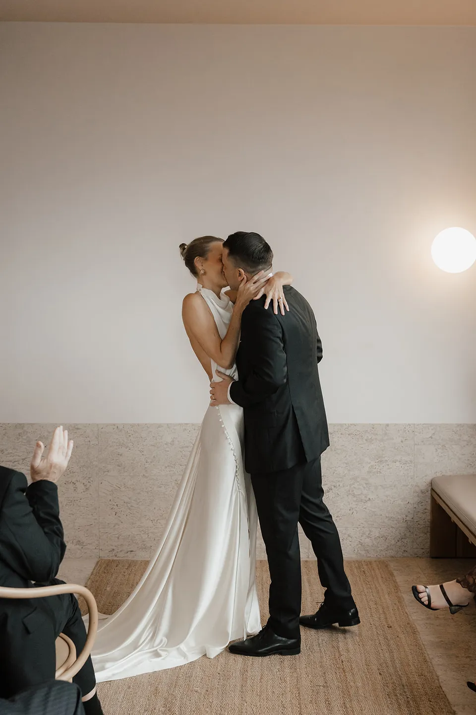 Clare and Matt kissing as their guests applaud in the suite at The Calile Hotel, Fortitude Valley, during their Elopement Collective elopement in Brisbane.