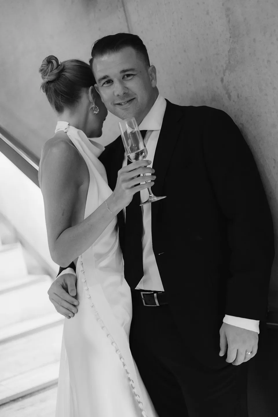 Black and white portrait of Clare leaning into Matt while holding champagne at The Calile Hotel, Fortitude Valley, during their Elopement Collective Brisbane elopement.