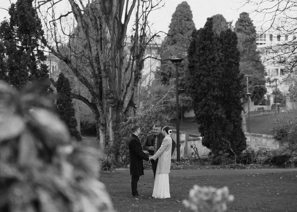 A black-and-white photograph of a couple standing together among tall trees in a garden.