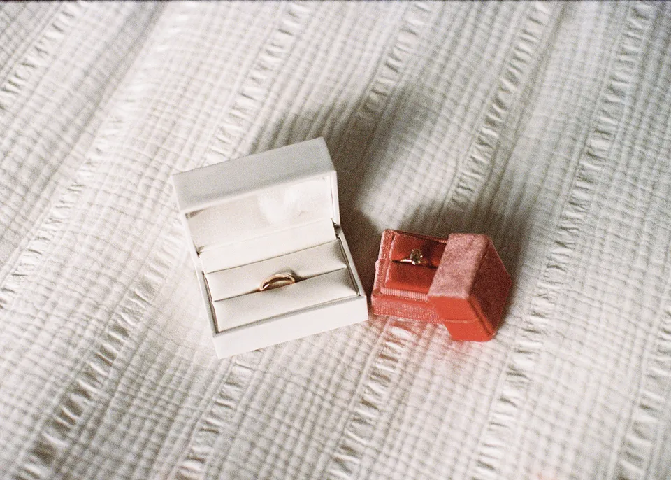 On 35mm film: Wedding rings in white and orange velvet boxes on a textured white bedspread. At Fig Tree Villa in Ewingsdale, Byron Bay, for an Elopement Collective elopement. Photograph by Bulb Creative.