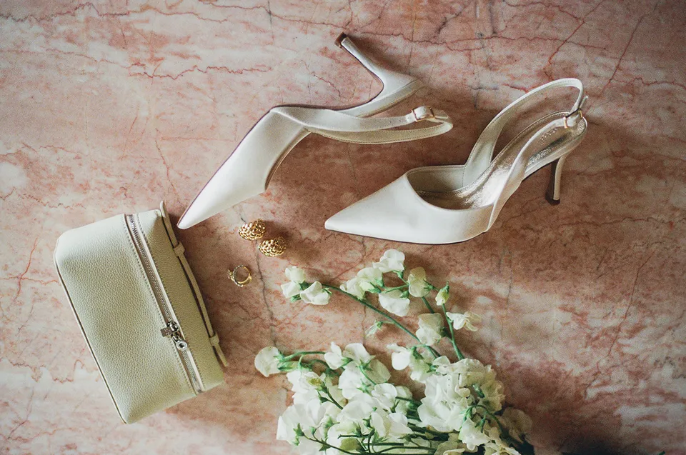 Ivory heels, a pale bag, gold jewellery and white flowers on pink stone at The Calile Hotel, Fortitude Valley, for an Elopement Collective Brisbane elopement.
