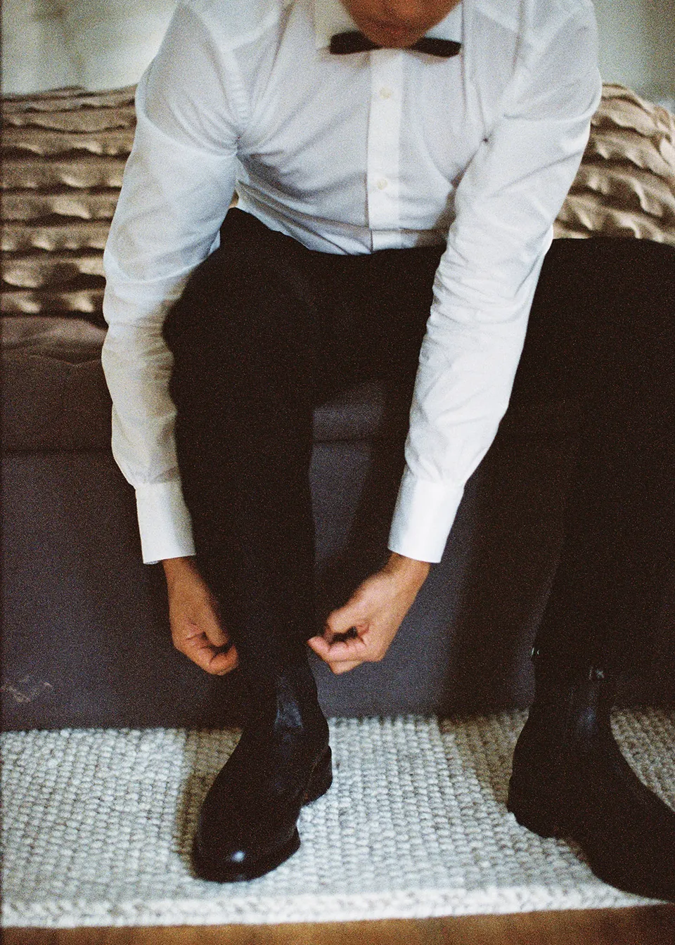 On 35mm film: Close-up of Jonathan adjusting his trouser leg above a black boot. At Fig Tree Villa in Ewingsdale, Byron Bay, for an Elopement Collective elopement. Photograph by Bulb Creative.