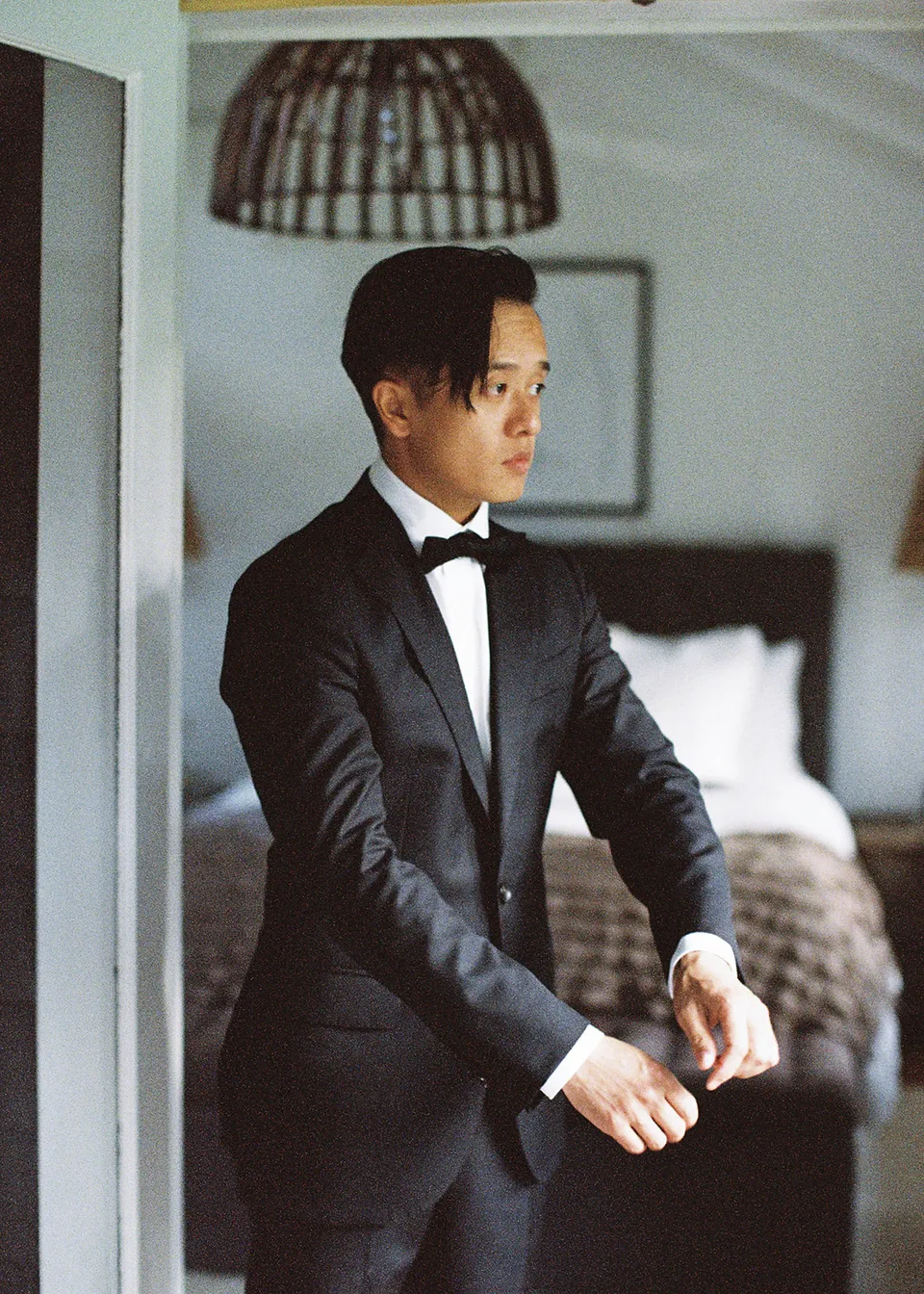 On 35mm film: Jonathan adjusting his cuff in the softly lit bedroom. At Fig Tree Villa in Ewingsdale, Byron Bay, for an Elopement Collective elopement. Photograph by Bulb Creative.
