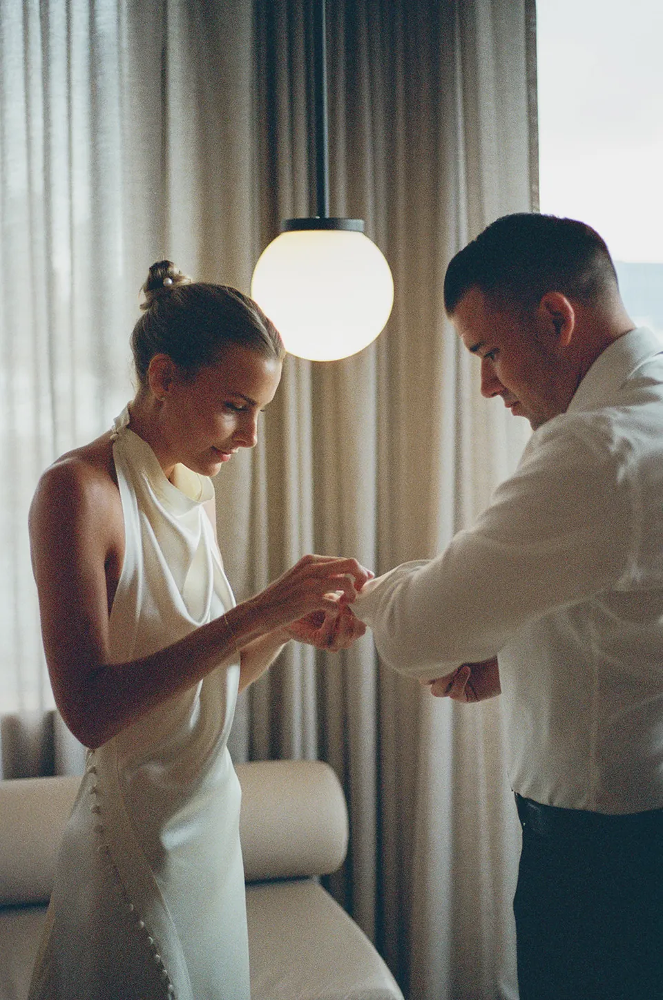 Clare and Matt getting ready together beside a window at The Calile Hotel in Fortitude Valley for their Elopement Collective elopement in Brisbane.