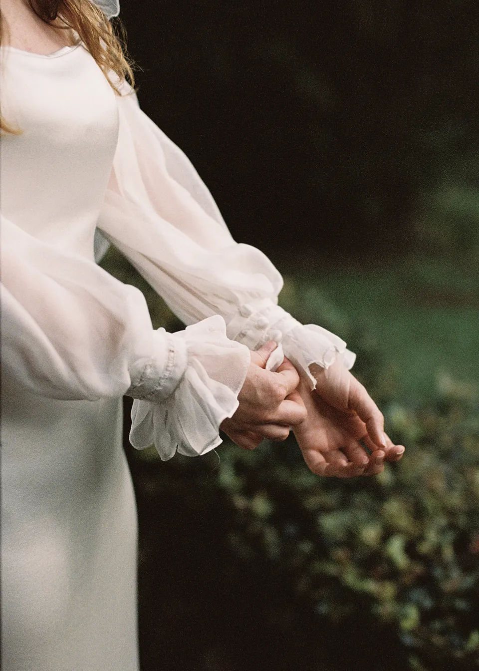 On 35mm film: Close-up of Elyse's folded hands and sheer sleeves outdoors. At Fig Tree Villa in Ewingsdale, Byron Bay, for an Elopement Collective elopement. Photograph by Bulb Creative.