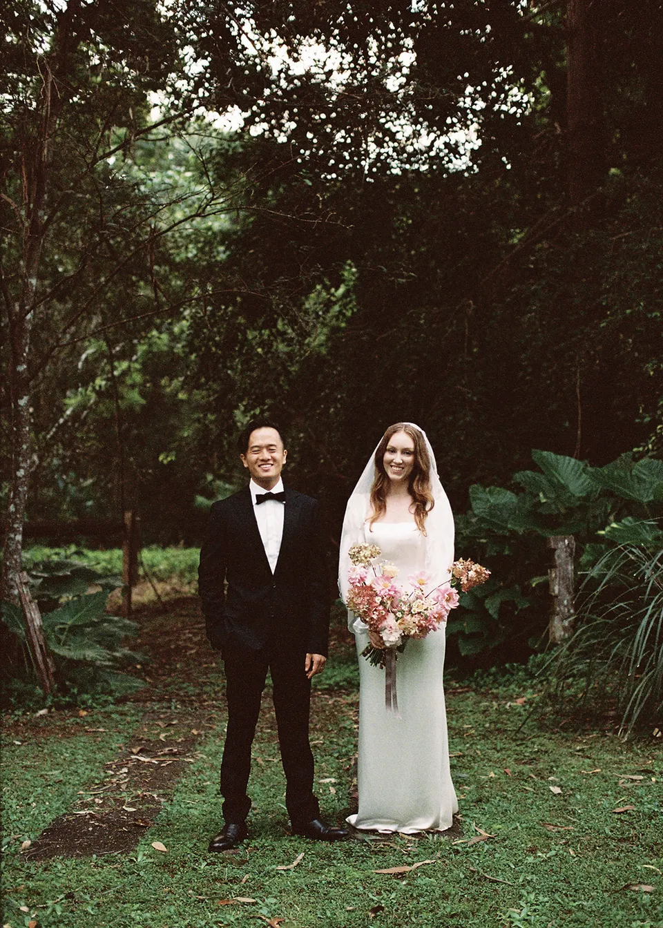 On 35mm film: Elyse and Jonathan standing side by side beneath the trees. At Fig Tree Villa in Ewingsdale, Byron Bay, for an Elopement Collective elopement. Photograph by Bulb Creative.