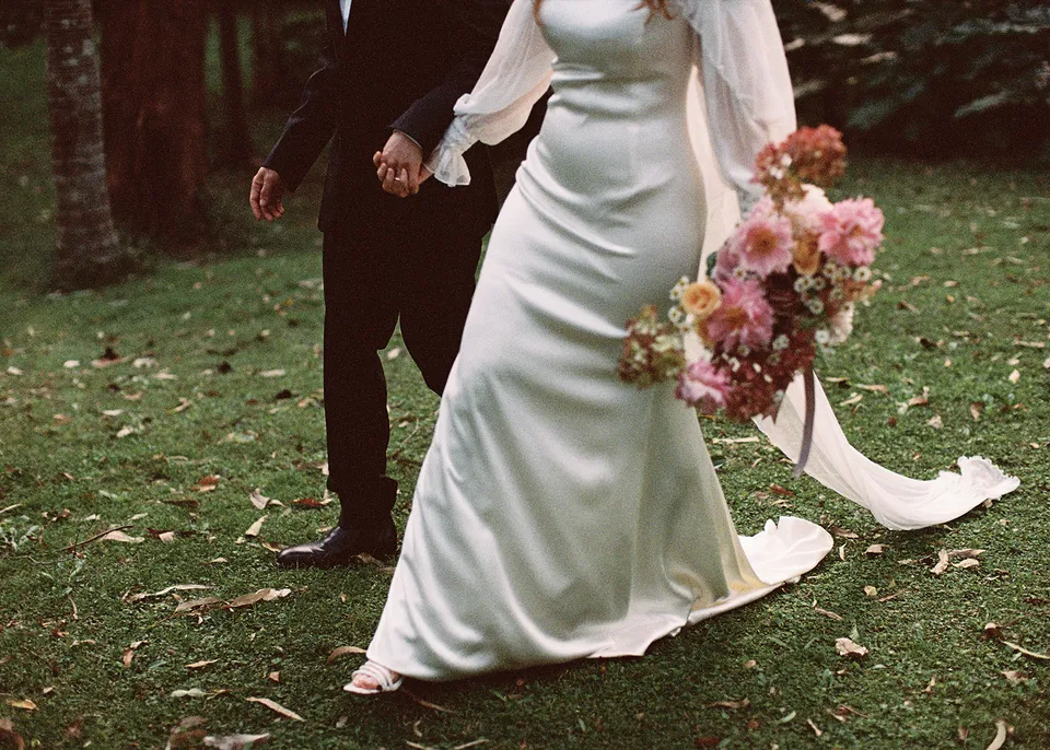 On 35mm film: Detail of Elyse's dress, bouquet and veil as she walks with Jonathan, with flowers by The Perfect Party Co. At Fig Tree Villa in Ewingsdale, Byron Bay, for an Elopement Collective elopement. Photograph by Bulb Creative.