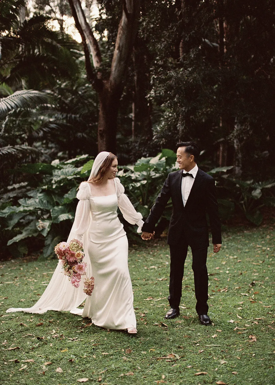 On 35mm film: The couple holding hands and looking at each other on the lawn. At Fig Tree Villa in Ewingsdale, Byron Bay, for an Elopement Collective elopement. Photograph by Bulb Creative.