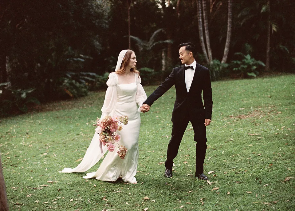 On 35mm film: Elyse looking towards Jonathan as they stroll with her bouquet, with flowers by The Perfect Party Co. At Fig Tree Villa in Ewingsdale, Byron Bay, for an Elopement Collective elopement. Photograph by Bulb Creative.